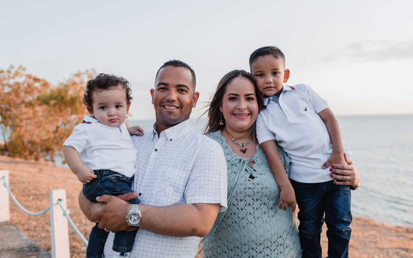 man and woman holding two sons in front of beach