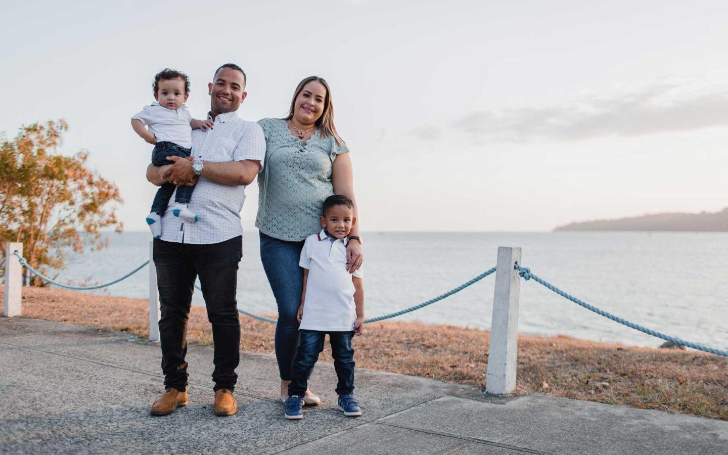 man and woman holding two sons in front of beach
