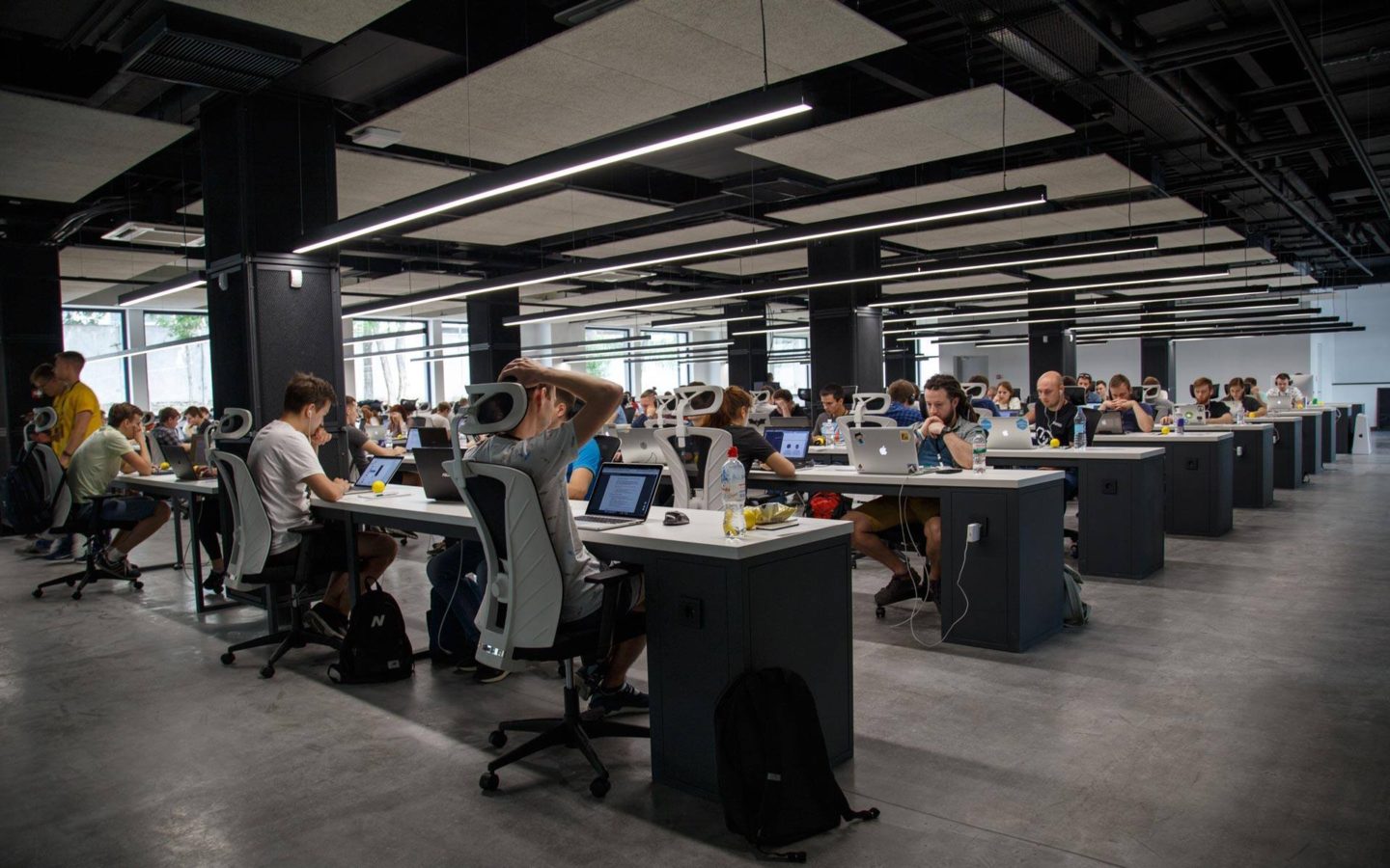 large modern office with rows of people sitting with laptops at black and white desks