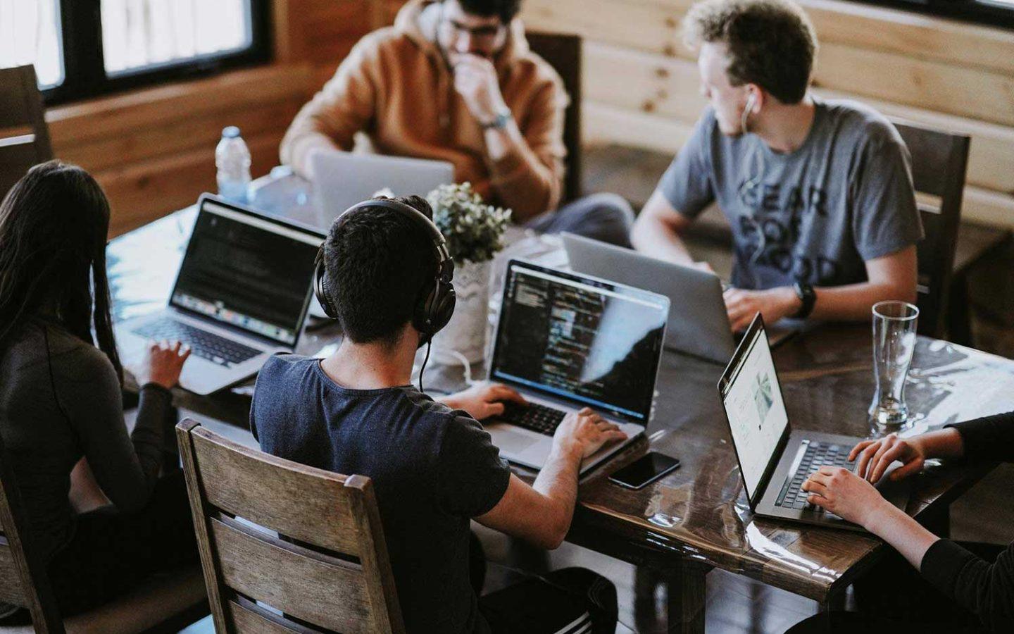 five people with laptops sitting around large desk